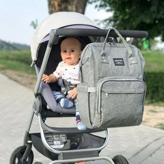 Sac a langer gris attaché à une poussette et bébé qui sourit