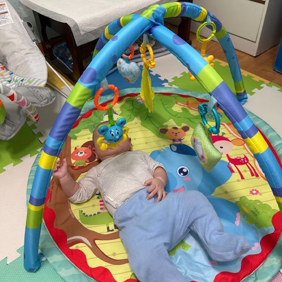 tapis d'éveil bleu, mauve et vert avec bébé sur le dos